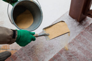 Injury prevention. Hand in green glove sprinkles sand on a winter path with a small shovel and bucket